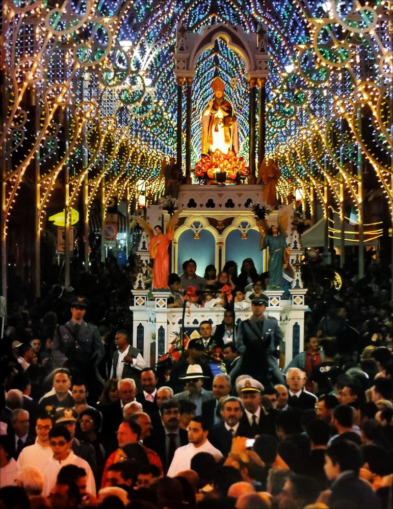 <div class="ql-editor"><div>La digitalizzazione di questa immagine, scattata nel 2012, mostra il momento solenne della discesa del Carro trionfale con la Statua del Patrono Erasmo, accompagnata da una folla di devoti in festa nella cittadina di Santeramo in Colle (BA).</div><div> La Festa Patronale in onore di Sant’Erasmo si celebra il 2 giugno ed è uno degli appuntamenti più sentiti dalla comunità. La giornata è ricca di eventi religiosi e civili che si susseguono nell’arco dell’intera giornata.</div><div>Al mattino si apre con la solenne celebrazione eucaristica presieduta dal Vescovo, alla presenza delle autorità civili e militari e di numerosi fedeli. Segue il tradizionale rito della consegna delle chiavi al Santo Patrono, ...
