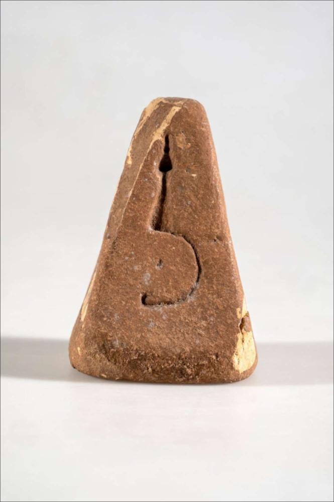 <div class="ql-editor"><div>Questo manufatto è un peso da telaio in terracotta, appartenente a un gruppo di quattro esemplari simili per impasto, colore dell’argilla e stato di conservazione. I quattro pesi furono consegnati nel 1935 al Museo Castromediano di Lecce dal reverendo Stanca, come documentato dagli archivi della SABAP Brindisi-Lecce. Il peso ha forma troncopiramidale e presenta un foro passante nella parte superiore, utilizzato per la sospensione. Su una delle facce è impressa a crudo la raffigurazione di una fibula ad arco semplice, ottenuta prima della cottura dell’oggetto.</div></div>