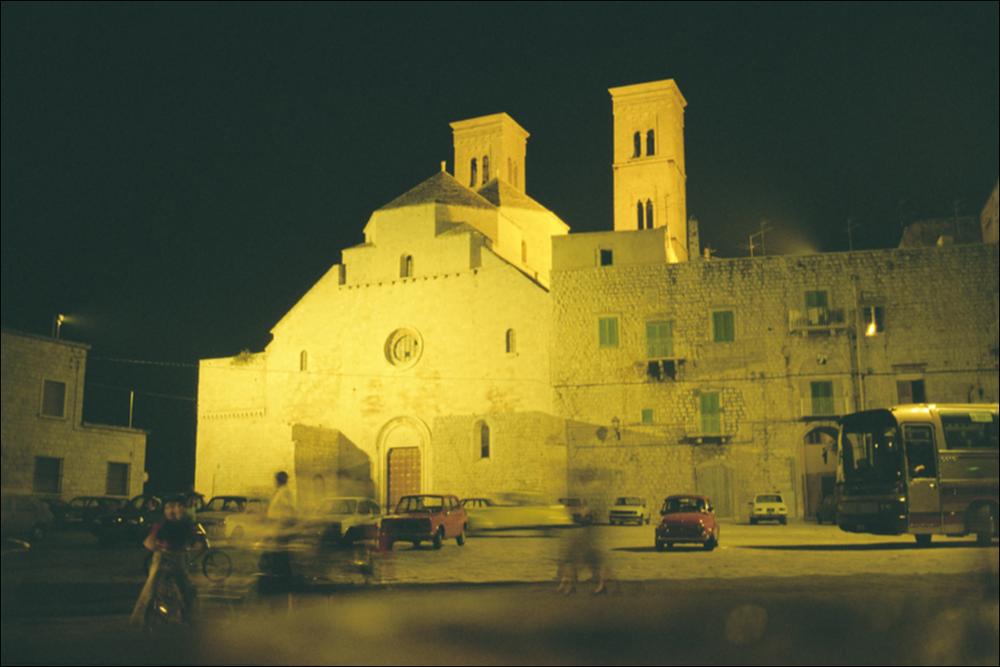 La fotografia è parte della ricca raccolta fotografica “Puglia per tutte le Stagioni” vol. 2, prodotta dall'Assessorato al Turismo e Industria Alberghiera della Regione Puglia e creata per raccontare la Puglia attraverso immagini diverse suddivise in 5 settori principali: Città e Paesi, Settimana Santa, Territorio, Feste – Sagre – Tradizioni, Mercati – Prodotti – Cucina. L'immagine immortala il Duomo di San Corrado, nobile di Baviera che dopo una carriere come guerriero durante crociate si ritirò in eremitaggio in una grotta in Terra di Bari, originariamente dedicato a Maria Santissima Assunta in Cielo, situato ai margini dell'antico borgo di Molfetta, di fronte al porto. Singolare esempio di architettura romanico-pugliese, fu costruito in due periodi differenti, presum...