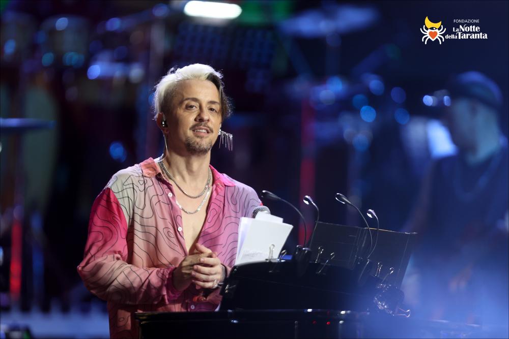 <div>Lo scatto ritrae <strong>Dardust</strong>, Maestro Concertatore e direttore artistico dell’edizione 2022, sul palco mentre guida l’orchestra e coordina la performance, con il ruolo di reinterpretare dei brani della tradizione salentina e nell’organizzazione musicale del Concertone.</div>...