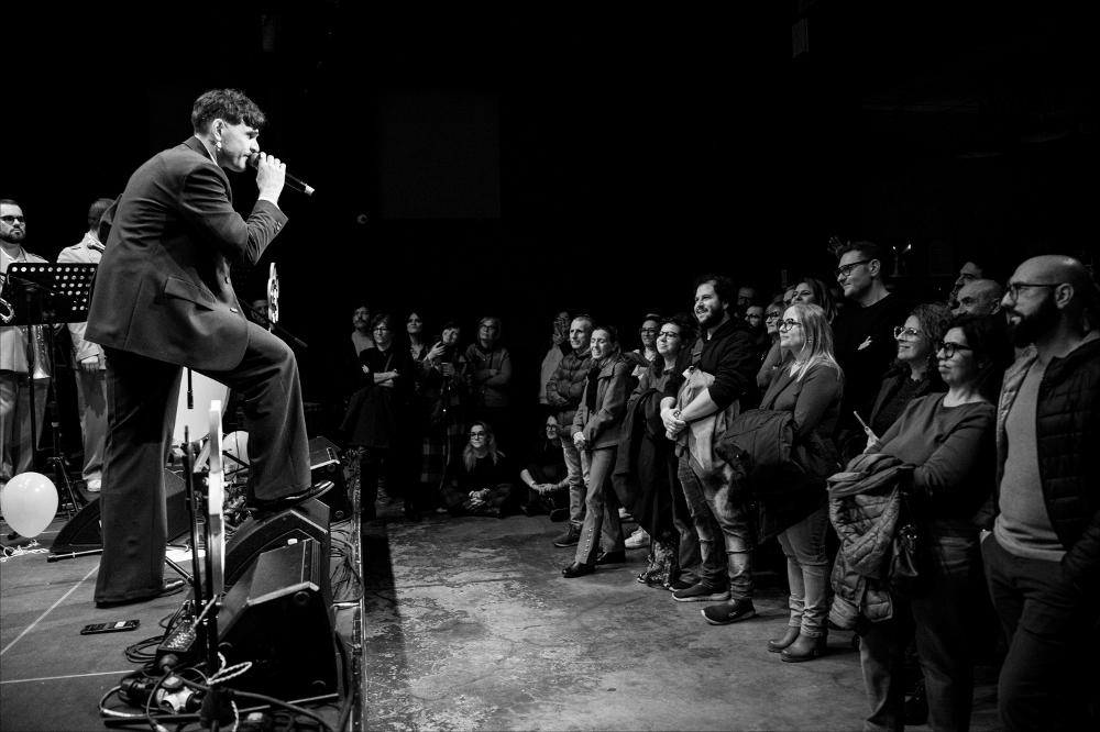 <div>Lo scatto ritrae Renzo Rubino insieme a La Sbanda, protagonisti della serata del 16 novembre allo Spazioporto/Cineporto di Taranto, nell’ambito di Cinzella d’Inverno – seconda parte del Cinzella Festival 2024.</div><div>Reduce dal successo del festival itinerante Porto Rubino, l’artista ha presentato il suo nuovo album “Il Silenzio Fa Boom”, un lavoro che prosegue l’esplorazione delle sue radici musicali abbracciando, al tempo stesso, la freschezza identitaria di una banda di paese. Con La Sbanda, Rubino inaugura un progetto unico nel panorama italiano: per la prima volta un cantautore pop intreccia la propria scrittura con arrangiamenti bandistici tradizionali, dando vita a un disco — e a un tour — in cui la mu...