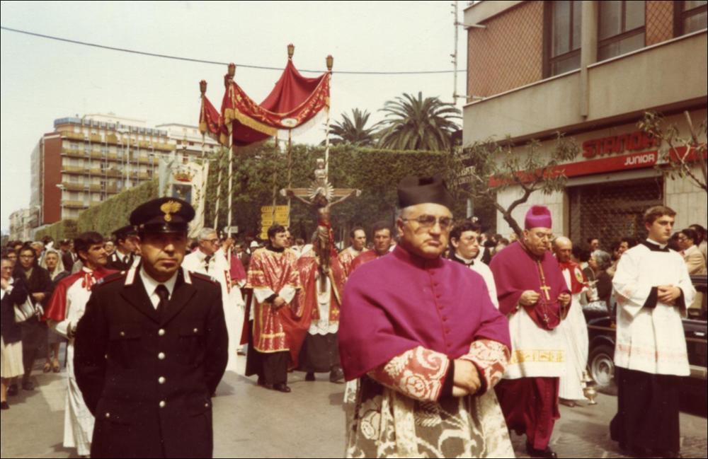 <div class="ql-editor"><div>Questa foto digitalizzata, scatto degli anni '80, immortala un momento della Processione per le vie cittadine in occasione della Festa Patronale del Santissimo Crocifisso di Colonna a Trani.</div><div>Questo festeggiamento rappresenta uno degli appuntamenti religiosi e civili più sentiti dalla comunità di Trani (BT), espressione profonda della fede e dell’identità cittadina.</div><div>Fulcro della celebrazione è il venerato Crocifisso ligneo custodito nel Santuario di Colonna, legato a un prodigio risalente al 1480, epoca dell’invasione turca in terra d’Otranto e del martirio degli Ottocento Cristiani. Secondo la tradizione, il Crocifisso, trafugato da pirati saraceni, venne sfregiato sul volto e gettato ...