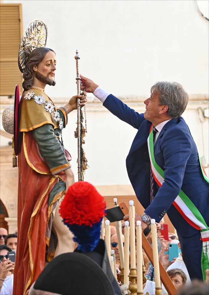 Il Sindaco consegna simbolicamente le chiavi della città a San Rocco, legandole al pastone della statua. Un gesto che rinnova la fiducia e l’affidamento della comunità alla protezione del Santo, custode di Noci e dei suoi cittadini.<div><br>
La festa patronale si celebra tradizionalmente il 16 agosto, giorno dedicato al Santo, mentre la solennità liturgica propria della comunità nocese ricorre nella prima domenica di settembre, cuore delle celebrazioni religiose e civili.
La devozione a San Rocco a Noci nasce agli inizi del Cinquecento, in un contesto segnato dal timore della peste che colpiva i territori vicini. Pur non essendo storicamente devastata dal contagio, la comunità sviluppò una profonda fiducia nella sua intercessione, riconoscendolo come protettore contro e...