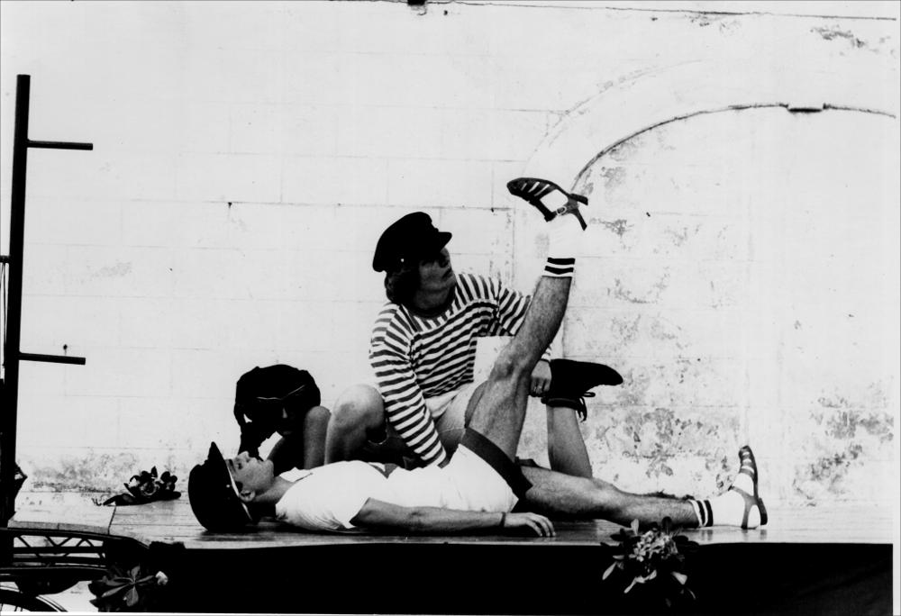 La fotografia in bianco e nero cattura un momento dello spettacolo “Summertime”, messo in scena nel 1987, nell'ambito della rassegna annuale “Aradeo e i Teatri”, un appuntamento con il teatro sperimentale che la compagnia Koreja, nata nel 1983 nel piccolo borgo salentino di Aradeo porta avanti sin dall'anno della sua fondazione. La performance ebbe come palcoscenico il suggestivo cortile del Castello "Tre Masserie", una struttura residenziale degli inizi del XX secolo situato tra gli ulivi della campagna di Aradeo. I personaggi principali della rappresentazione sono “vittime” di un mènage a tre durante le vacanze estive. Una spiaggia, due ragazze terribili e un ragazzo che, pur essendo fortemente attratto da loro, tenta in ogni modo, quasi con disperazione, di allontana...