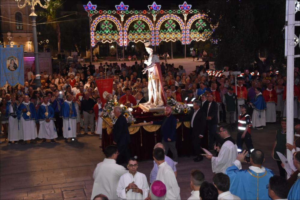<div class="ql-editor"><div>La fotografia documenta la processione del 2023 dedicata a <strong>San Ferdinando Re</strong> che attraversa le strade di San Ferdinando di Puglia durante la festa patronale. Al centro dell’immagine si distingue il simulacro del Santo portato in processione tra i fedeli, mentre il corteo religioso percorre le vie del paese.</div><div>Lungo il percorso sono disposti in ordine i membri delle confraternite mariane, riconoscibili per gli abiti cerimoniali: tuniche bianche accompagnate da mantelle celesti e mantelle rosse. La loro presenza, ordinata ai lati della strada, contribuisce a creare un suggestivo scenario devozionale e sottolinea la partecipazione organizzata delle confraternite alla celebrazione.</div><div><br></div><div>La festa ...