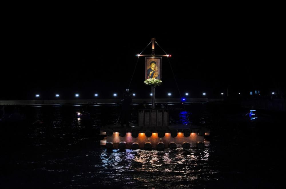 <div class="ql-editor"><div>La foto ritrae il suggestivo momento della rievocazione dell’arrivo dal mare della Madonna della Madia nel porto di Monopoli. Al centro della scena si distingue la <strong>zattera illuminata</strong>, sulla quale è collocata la sacra immagine della Madonna, mentre avanza lentamente sull’acqua sospinta dalle <strong>pale dei rematori</strong>.</div><div>L’imbarcazione procede verso la riva tra luci, riflessi sul mare e l’attesa dei fedeli, rievocando simbolicamente il miracoloso approdo della patrona e uno dei momenti più emozionanti della tradizione religiosa monopolitana.</div><div><br></div><div>La festa patronale in onore della Madonna della Madia, patrona di Monopoli, nasce dalla tradizione del <strong>11...