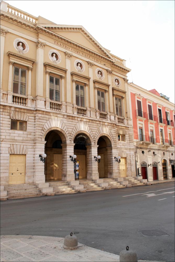 L'immagine è parte della campagna fotografica realizzata dalla fotografa Margherita Mirabella per Teatro Pubblico Pugliese, che con i suoi scatti ha ripreso le eleganti architetture e i rifiniti dettagli di alcuni dei più bei teatri pugliesi e di alcuni spettacoli teatrali portati in scena in questi ultimi anni. Lo scatto immortala la facciata esterna di Teatro Curci di Barletta, importante contenitore culturale cittadino intitolato al compositore Giuseppe Curci situato in pieno centro. L'aspetto attuale è quello del nuovo teatro, costruito interamente sul precedente e più antico teatro di San Ferdinando, per volontà del comune, che lo acquistò ordinandone l'abbattimento dopo il suo crollo parziale. I lavori iniziarono nel 1868 con la direzione dell'architetto Federico ...