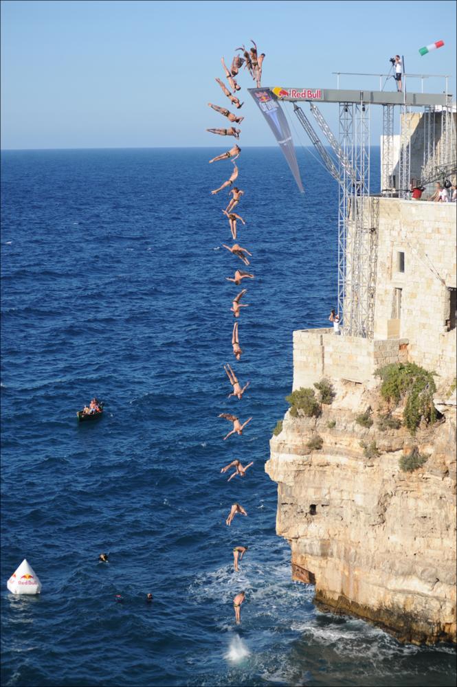 L'immagine digitale è una fotografia scattata nell'agosto del 2010 con luce pomeridiana dal fotografo Sergio Scagliola durante il Red Bull Cliff Diving World Series, l'ormai nota competizione internazionale di tuffi estremi da grandi altezze più famosa al mondo, creata nel 2009 dalla nota azienda di bibite, che si svolge in tutto il mondo. Adrenalina e sangue freddo contraddistinguono questa competizione, unica al mondo, nella quale tuffatori da tutte le nazioni gareggiano in scenari naturali mozzafiato che permettono agli sportivi di tuffarsi da un'altezza minima di 26 metri sul livello del mare. Dal 2008, la Red Bull Cliff Diving fa tappa anche nella suggestiva ambientazione naturale di Polignano a Mare, cittadina dal caratteristico nucleo storico abitativo arroccato ...