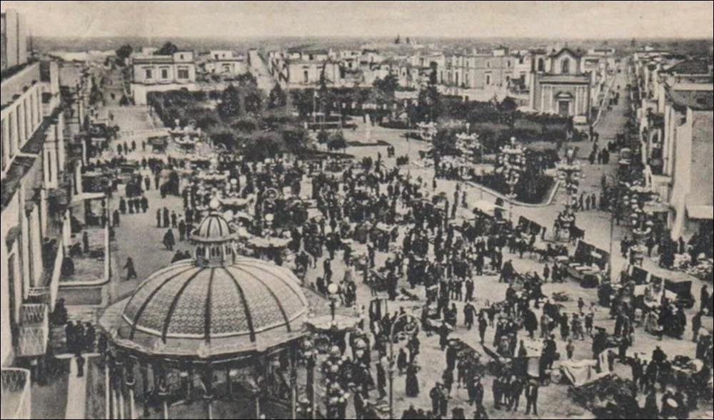 <div class="ql-editor"><div>Cartolina storica che mostra la piazza principale addobbata a festa, con la cassarmonica in primo piano e la folla che passeggia nella villa comunale dell’epoca. Sullo sfondo si nota la <strong>Chiesetta rettoria di San Luigi Gonzaga</strong>, la cui facciata è scandita da quattro lesene, colonne piatte applicate al muro che conferiscono ritmo e armonia alla struttura.</div><div><br></div><div>La Festa Patronale di Bitritto in onore di <strong>Santa Maria di Costantinopoli</strong> è l’evento più importante per la comunità e affonda le sue radici nel XVI secolo, dopo la pestilenza del 1528-29, quando i cittadini fecero voto alla Madonna promettendo la costruzione di una chiesa in suo onore.</div><div>Nel 1656, ...