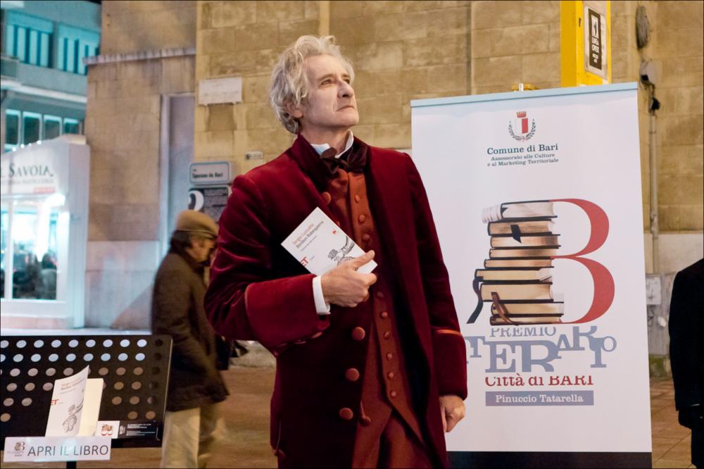 L'immagine digitale in oggetto documenta una delle azioni di teatro urbano, messe in scena dall'Associazione Fibre Parallele, durante l'evento "Premio Letterario Città di Bari", dell'edizione 2010. La fotografia è stata scattata all'attore barese Pinuccio Sinisi, tra gli attori più conosciuti nel panorama artistico locale che ha rappresentato la Puglia in molti lavori teatrali e cinematografici a livello nazionale. Per l'occasione interpretava la lettura del libro "Bonbon Robespierre” di Sergio Luzzato", edito da Einaudi, vincitore del del Premio Letterario Città di Bari nella sezione saggistica. Non tutti sanno che il più famoso Robespierre aveva un fratello, Augustin, soprannominato Bonbon dagli amici; un personaggio minore della storia della Rivoluzione francese, ma ...
