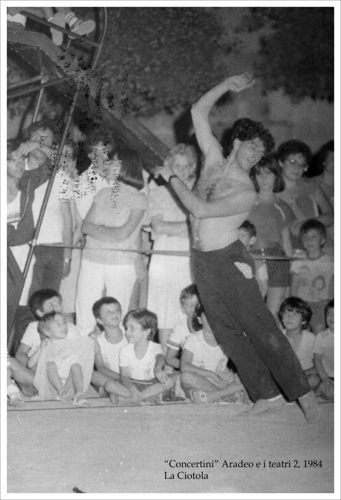 La fotografia in bianco e nero immortala un momento dello spettacolo teatrale “Tinta unita indoor” nell'ambito della rassegna annuale “Aradeo e i Teatri” del 1984, alla seconda edizione con il titolo “concertini”, un appuntamento con il teatro sperimentale che la compagnia nata nel 1983 nel piccolo borgo salentino di Aradeo porta avanti sin dall'anno della sua fondazione. Lo spettacolo è messo in scena, nella piazzetta San Giovanni, dalla compagnia teatrale La ciotola di Verona, nata nel 1976 dall'incontro tra gli attori del “Libre teatro libre” argentino e alcuni giovani attori di Verona. “Tinta unita”, per la regia dell'attrice argentina Graciela Ferrari che dal 1982 assunse la direzione della compagnia, ha una trama che alterna poesia ed umorismo, gioco e dramma, qua...