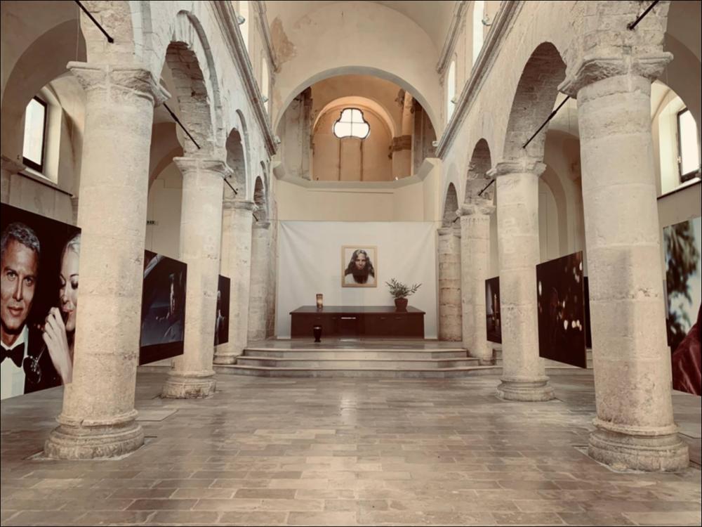 La chiesa dei SS. Pietro e Paolo, posta nelle vicinanze dell’aristocratico Palazzo Palmieri, è stata per secoli conosciuta con la fama di chiesa più aristocratica del paese, considerata la frequentazione di nobili famiglie. L’edificio attuale dovrebbe risalire al XVIII secolo, anche se la facciata è cinquecentesca. L’interno presenta tre navate con cinque arcate e cinque colonne per navata. Dopo varie riedificazioni, fu chiusa definitivamente al culto nel 1955. Durante il festival PhEST diventa un ambiente espositivo di eccellenza. Nel 2021 ha ospitato la mostra di Phillip Toledano (Londra, 1968). Gli scatti raccontano le sue visioni del futuro, possibilità del suo destino ricavate da una sua ricerca in base a predisposizioni genetiche e scelte di vita....
