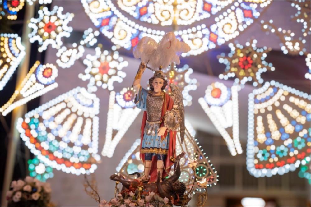 <div class="ql-editor"><div>La fotografia mostra frontalmente l’effige di <strong>San Michele Arcangelo</strong> durante la processione della Festa Patronale di Palese nel 2024. La statua raffigura l’Arcangelo con spada e armatura, simboli della sua funzione di difensore del bene, e il mantello che ricade sulle spalle, mentre ai suoi piedi un uomo incatenato rappresenta il male sconfitto. Dietro la statua si intravedono le luminarie, catturando l’atmosfera solenne e suggestiva dell’evento.</div><div><br></div><div>La Festa Patronale di Palese, borgo a nord di Bari, è dedicata a San Michele Arcangelo, celeste protettore della comunità. Si celebra ogni anno nei primi giorni di agosto e rappresenta il momento più alto e identitario de...