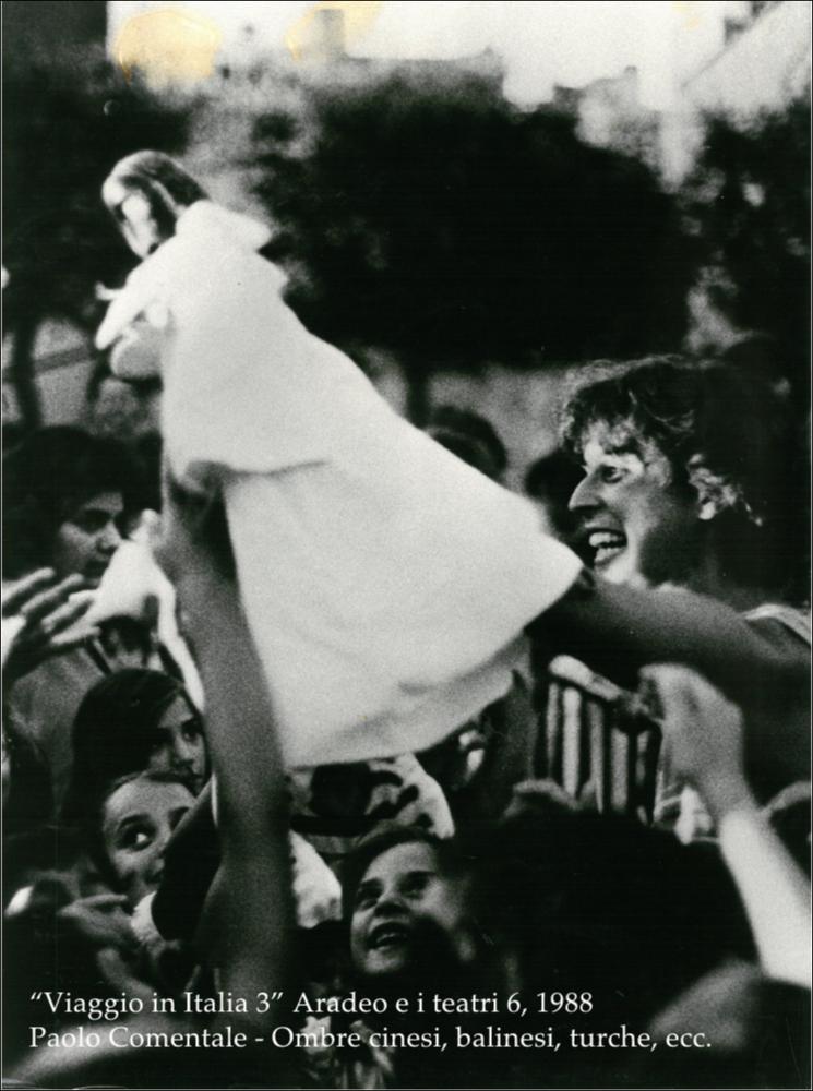 La fotografia in bianco e nero cattura un momento dello spettacolo di Paolo Comentale, rappresentata nel 1988, nell'ambito della rassegna annuale “Aradeo e i Teatri”, un appuntamento con il teatro sperimentale che la compagnia del Teatro Koreja, nata nel 1983 nel piccolo borgo salentino di Aradeo porta avanti sin dall'anno della sua fondazione. L'azione teatrale fu messa in atto nel cortile delle "Tre Masserie", una struttura residenziale degli inizi del XX secolo tra gli ulivi della campagna di Aradeo che divenne la sede operativa della compagnia, durante la quale l'attore si trasformò in un burattinaio "colto" presentando delle variazioni sul tema di Pulcinella, unendo delle suggestioni provenienti dal mondo esotico, come ombre cinesi, balinesi e turche. La rassegna, ...