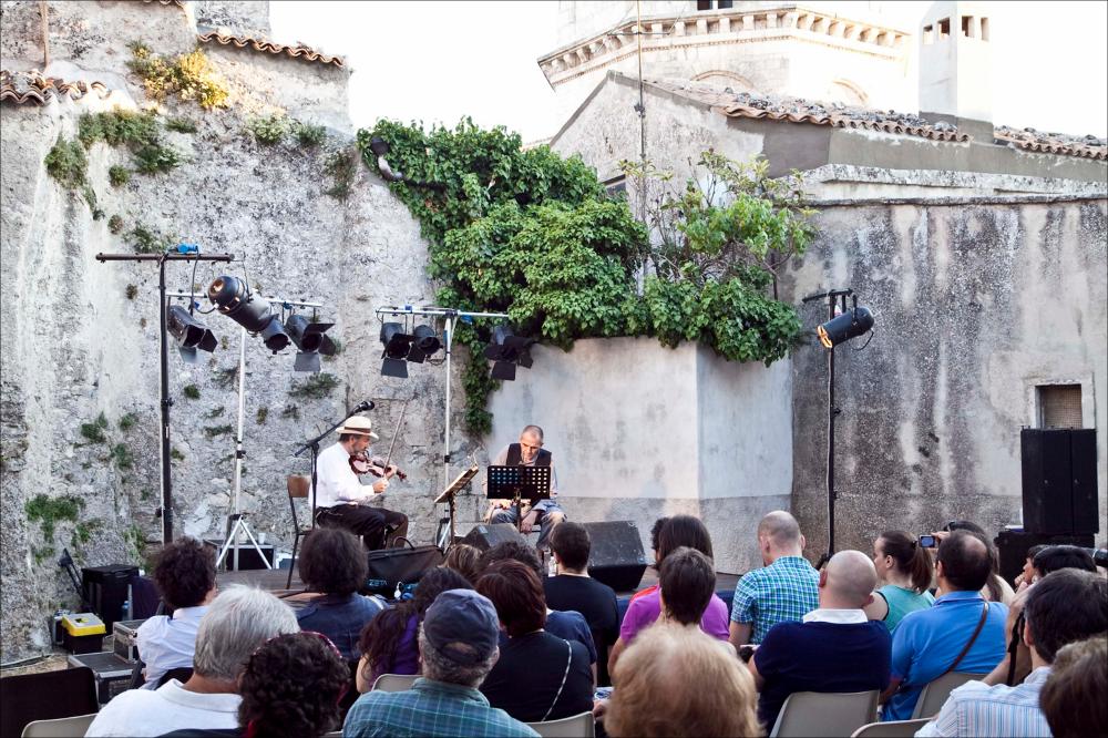 L'immagine digitale in oggetto è parte della collezione “Puglia Green Hour” nata dall'omonimo progetto di Teatro Pubblico Pugliese. Fu organizzato su un calendario fitto e intenso di spettacoli programmati tra giugno e luglio 2012 all'interno dei Parchi Regionali della Puglia, per parlare di arte, musica, teatro e filosofia ispirati dalle bellezze primordiali del paesaggio pugliese in aree territoriali spesso dimenticate o poco valorizzate. La fotografia documenta uno dei momenti del recital intitolato “Bella gente d'Appennino” realizzato a Monte Sant'Angelo, all'interno del Complesso Monumentale del Santuario di San Michele Arcangelo (sito UNESCO) grazie alla collaborazione tra FestambienteSud, Teatro Pubblico Pugliese e Puglia Sound. La performance, interpretata dal c...