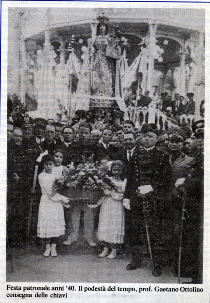 La fotografia storica immortala uno dei momenti più significativi della Festa Patronale della Madonna della Croce, celebrata a Triggiano negli anni Quaranta. In primo piano si distingue il Podestà dell’epoca, Gaetano Ottolino, solennemente impegnato nella cerimonia di consegna delle chiavi della città alla Patrona, gesto simbolico di affidamento e devozione dell’intera comunità.
Le origini della devozione alla Madonna della Croce risalgono al XVI secolo, quando, fuori dall’antico abitato, venne edificata un’edicola sacra decorata con un’immagine “miracolosa” ad opera dei cosiddetti “homini de fora”, ossia contadini e braccianti che ogni giorno passavano di lì per andare a lavorare nei campi.
Una guarigione ritenuta miracolosa, avvenuta proprio nei pressi di quell’edicol...