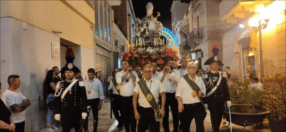 La fotografia ritrae il gruppo di portatori volontari che trasporta a spalla il simulacro del santo patrono San Sabino lungo le strade di Canosa. Accanto al corteo si distinguono i Carabinieri in divisa. La scena esprime devozione, senso di responsabilità e partecipazione collettiva. 

<div><br>La festa patronale di San Sabino si celebra ogni anno il 1° agosto a Canosa di Puglia e rappresenta un momento centrale della vita culturale e religiosa della città. La ricorrenza rievoca la traslazione del corpo del santo dalla Basilica di San Pietro alla basilica a lui dedicata, un evento che unisce fede, storia e tradizione popolare.
La festa è caratterizzata da un forte coinvolgimento della comunità: quasi tutti i cittadini canosini, così come i fedeli residenti fuori città, ...