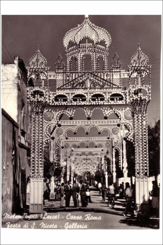In questa foto storica del 1950 vediamo Corso Roma a Melendugno, allestita con luminarie colorate in occasione della Festa Patronale di San Niceta.
La Festa Patronale di San Niceta Goto Martire, istituita nel 1740, si celebra nei giorni 15 e 16 Settembre a Melendugno in provincia di Lecce. Il rito religioso parte nove giorni prima della Festa, con delle celebrazioni eucaristiche presso la chiesa Madre e in forma esclusiva viene celebrata la santa messa in rito bizantino presso l’Abbazia di San Niceta situata in Melendugno sin dal 1167, riconosciuta appunto come uno dei più importanti riferimenti storici del territorio.
Il giorno della vigilia della Festa, come da tradizione pluricentenaria, al termine della Santa Messa, i fedeli accompagnati da un concerto bandistico, t...