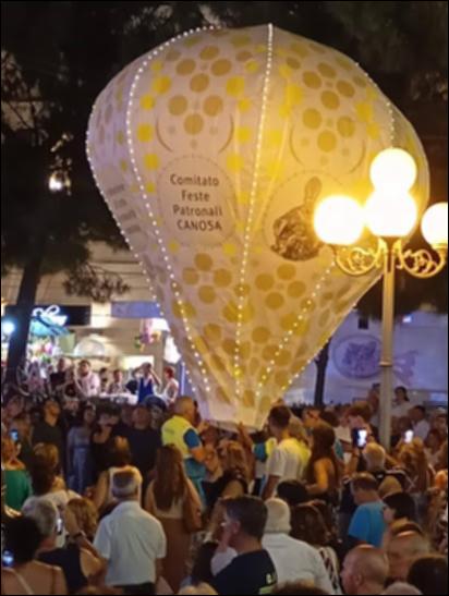 L’immagine ritrae il momento del lancio del pallone aerostatico dedicato al santo patrono San Sabino, gesto simbolico che apre o accompagna i momenti culminanti della festa. Il pallone, gonfiato ad aria calda, viene trattenuto dai volontari e poi lasciato salire lentamente verso il cielo tra gli sguardi della folla. <div><br>La festa patronale di San Sabino si celebra ogni anno il 1° agosto a Canosa di Puglia e rappresenta un momento centrale della vita culturale e religiosa della città. La ricorrenza rievoca la traslazione del corpo del santo dalla Basilica di San Pietro alla basilica a lui dedicata, un evento che unisce fede, storia e tradizione popolare.
La festa è caratterizzata da un forte coinvolgimento della comunità: quasi tutti i cittadini canosini, così come i...
