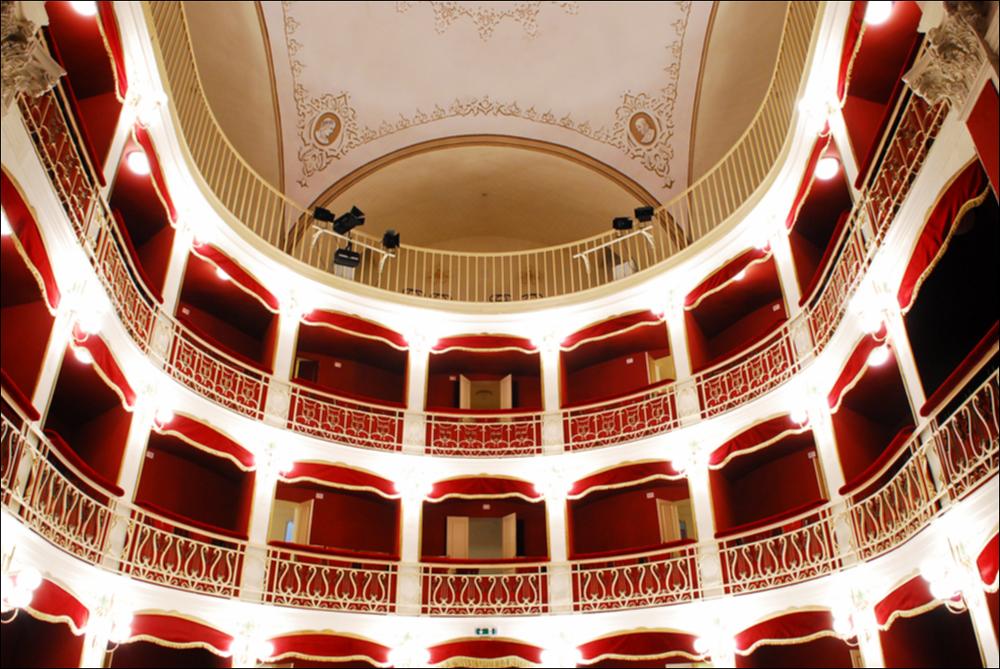 L'immagine è parte della campagna fotografica realizzata dalla fotografa Margherita Mirabella per Teatro Pubblico Pugliese, che ha ripreso nei suoi scatti le eleganti architetture e i rifiniti dettagli di alcuni dei più bei teatri pugliesi e alcuni degli spettacoli teatrali portati in scena in questi ultimi anni. È una bella panoramica dell'interno del Teatro Comunale di Nardò, situato in Via Mauro Manieri, piccolo gioiello culturale ottocentesco della città salentina. Dopo l'Unità d'Italia, l'esigenza di avere un Teatro Comunale per la popolazione locale spinse la Prefettura ad affidare l'incarico per la sua realizzazione. Nel 1893, fu accolto il progetto dell'Ing. Quintino Tarantino e i lavori iniziarono nello stesso anno su alcuni immobili demoliti in largo Carmine. ...