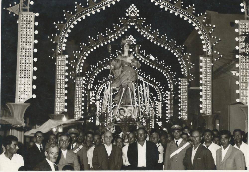 <div class="ql-editor"><div>L'immagine digitalizzata risale agli anni '70 e immortala un momento molto significativo della Festa Patronale di Alezio: la statua di Santa Maria della Lizza viene portata in Processione da una folla di devoti.</div><div>Questa Festa rappresenta il momento più solenne e significativo del calendario religioso e civile della comunità di Alezio, piccolo centro del Salento in provincia di Lecce. Si celebra ogni anno il 14, 15 e 16 agosto e si distingue per la profonda devozione popolare, l’intensità delle celebrazioni liturgiche e la ricchezza delle manifestazioni civili e culturali che la accompagnano.</div><div>Fulcro della festa sono i riti religiosi in onore di Santa Maria della Lizza, Patrona di Alezio, venerata nell...