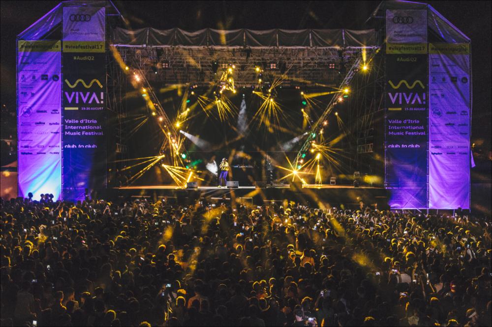 L’edizione 2017 del "VIVA" Festival intende regalare notti magiche alla Valle d’Itria e al pubblico pugliese, nazionale e internazionale. Tra i protagonisti di spicco di questa edizione troviamo Nicolas Jaar (live), Dj Shadow, Madlib, Todd Terje, Ghali, Lorenzo Senni, Kelly Lee Owens, Jolly Mare e Populous (e altri) si aggiungono John Talabot, Rroxymore, Don’t DJ, Jolly Mare, Zippo e Fides. Oltre agli show, ospita una serie di incontri condotti da Carlo Pastore, storico presentatore radiofonico di Babylon su Rai Radio 2, nonché direttore artistico di MI AMI Festival. La fotografia mostra un concerto svolto durante il Festival dove il numeroso pubblico partecipa all'evento. Le luci dominano l'intera scena....