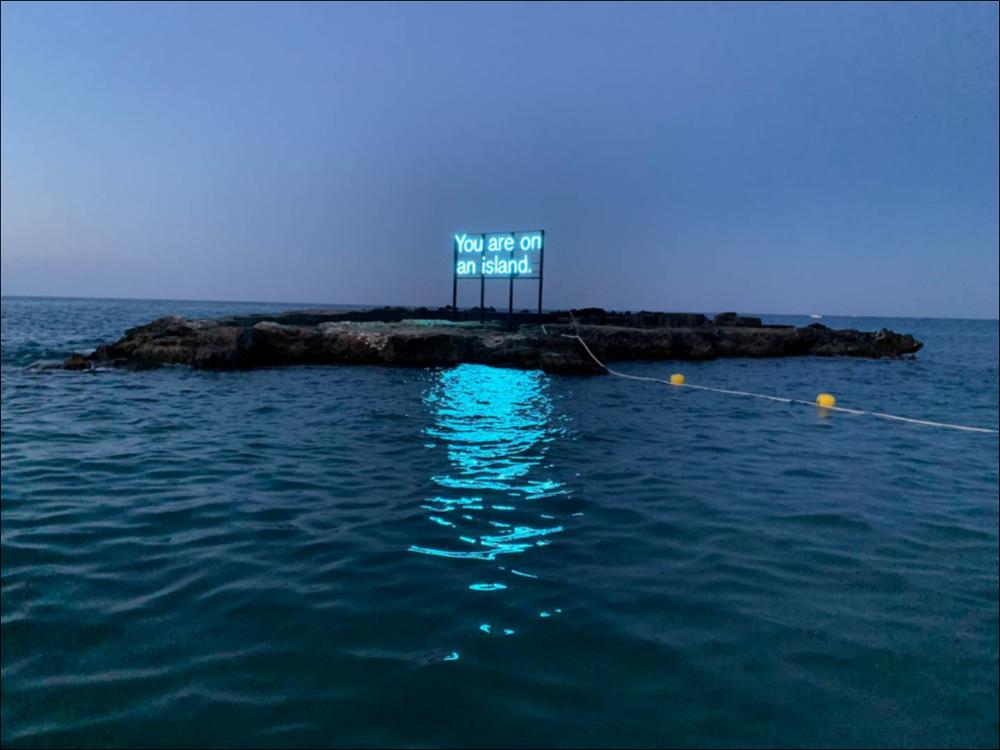 Sul piccolo isolotto di fronte a Cala Porta Vecchia, è visibile l'installazione di Alicia Eggert. È un'insegna al neon il cui messaggio è animato dalla parola "ON" che lampeggia ad intervalli regolari, trasformando un'affermazione inizialmente ovvia, in un'indagine riflessiva e filosofica. Il segno spinge l'osservatore a pensare sia dentro che fuori di se. L'artista invita a meravigliarsi del mondo nel quale ci si trova e del ruolo che si svolge in esso, riflettendo sulla consistenza di sé nel mondo, del qui ed ora.
“You are more like an island than you can perceive.” 
...