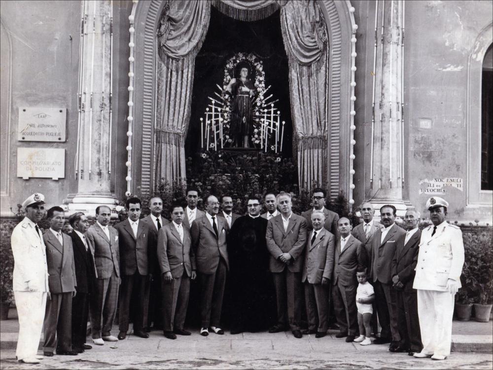 <div class="ql-editor"><div>Lo scatto fotografico del 1960 cattura un’immagine della cosiddetta “macchina di San Nicola”, un altare all’aperto abbellito da luminarie e addobbi.</div><div>I festeggiamenti in onore di San Nicola il Pellegrino, Patrono di Trani, morto in città nel 1094, costituiscono uno degli appuntamenti più importanti della tradizione religiosa e civile tranese.</div><div>La festa patronale si svolge ogni anno nei giorni di sabato, domenica e lunedì della prima settimana di agosto ed è articolata in tre momenti principali.</div><div>Il sabato sera l’effigie lignea del Santo, custodita presso il Santuario di Santa Maria di Colonna, viene trasportata via mare fino al porto di Trani su un’imbarcazione...