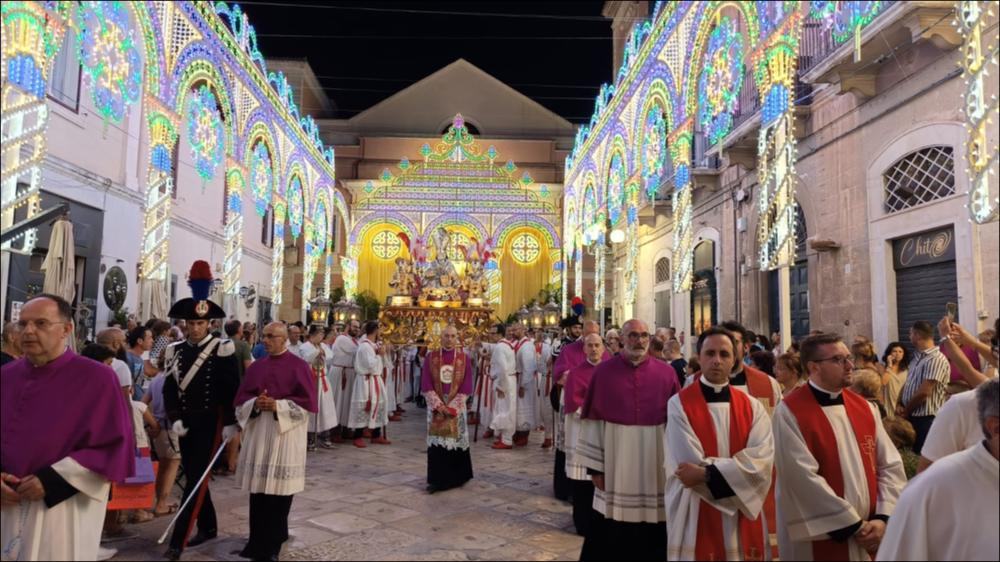 <div class="ql-editor"><div>Lo scatto immortala un momento della festa patronale dei Santi Martiri Mauro Vescovo, Sergio e Pantaleo, celebrata a Bisceglie: la statua dei santi avanza in processione tra la folla devota, avvolta dalla luce delle luminarie che animano lo spazio urbano.</div><div>La festa patronale, che si svolge la seconda domenica di agosto, rappresenta un elemento identitario forte per la comunità di Bisceglie, richiamando in città numerosi biscegliesi residenti in altre regioni e all’estero. Essa nasce dall’intreccio profondo tra storia religiosa e storia civile: a partire dal XII secolo, con l’adozione dei santi martiri come patroni, la città divenne un importante punto di riferimento per i pellegrini diretti in Terra S...