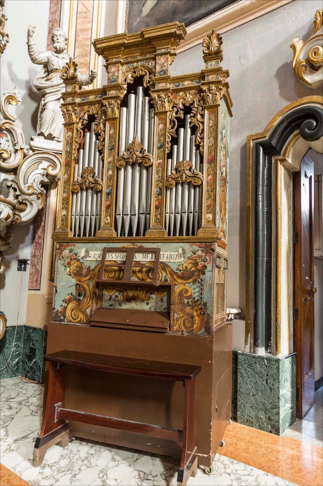 L’organo raffigurato nell'immagine digitale è collocato nella collegiata di S. Nicola (o Chiesa della Presentazione del Signore) a Maglie. La collegiata si fa risalire ai primi anni del secolo XVI quando ancora si praticava il rito greco; nel 1681 è già attestato il rito latino e, a seguito dello stato del degrado dell’edificio e di un terremoto del 1743, fu completamente demolita e ricostruita nel 1765. I lavori di costruzione sono attribuiti al mastro muratore Giuseppe Serio con la collaborazione delle maestranze salentine, i Morgese e i Fasano. Successivo è stato l’intervento del capomastro Giuseppe Negro di Parabita e dell’architetto Felice De Palma di Alessano, al quale si assegna il disegno della facciata. All’interno l’altare maggiore è opera delle maestranze ost...