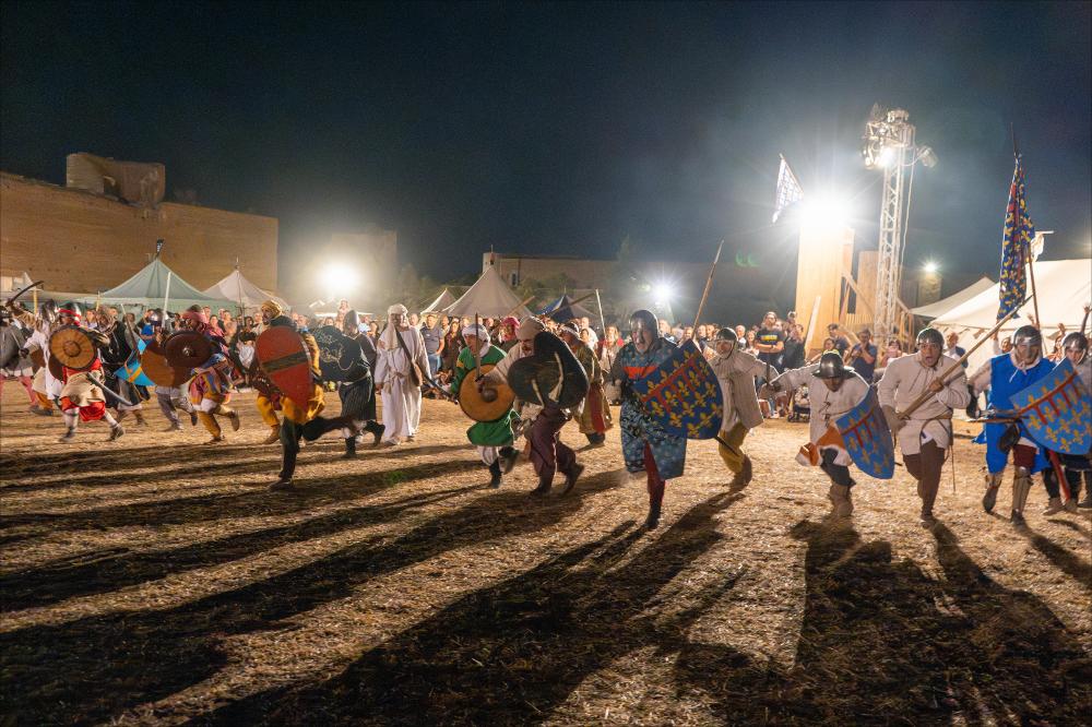 <div>Prima giornata del Villaggio Medioevale a Lucera. La fotografia ritrae la carica degli armati delle Cinque Porte Storiche, con scudi colorati e spade sguainate, durante la rievocazione storica <em>“Corradino e la rivolta nel regno”</em>, primo episodio del ciclo narrativo <em>“1268-1269 – L’assedio angioino di Lucera”</em>. L’azione si inserisce nel racconto dell’assedio che pose fine all’autonomia della <em>Luceria Saracenorum</em>, restituendo al pubblico uno spaccato di vita militare e quotidiana del XIII secolo. Sullo sfondo sono visibili gli accampamenti storici, momenti di falconeria e il lancio della palla infuocata dal trabucco, elemento spettacolare che conclude la serata.</div><div><br></div><div>Dall&...
