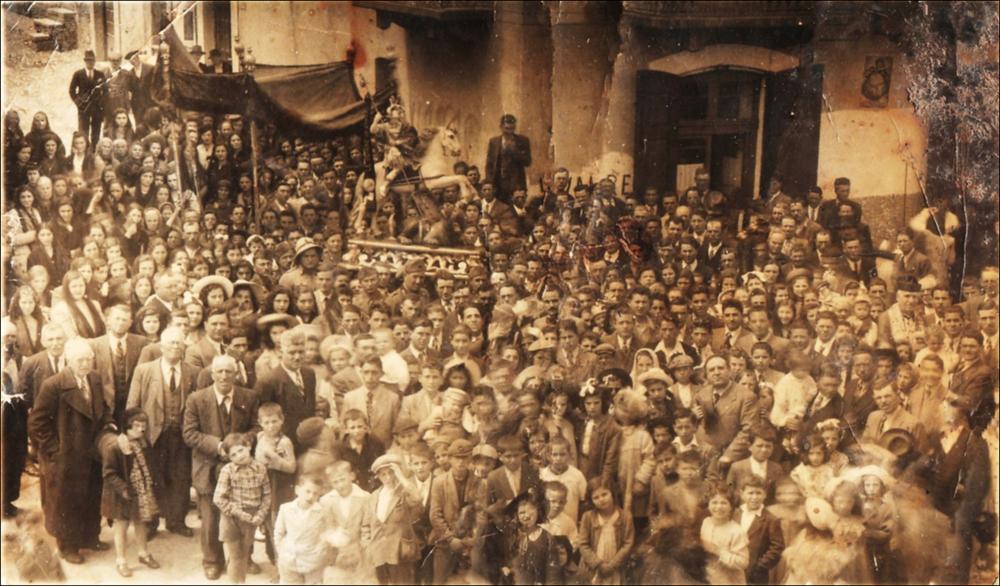<div><strong>Foto storica (fine XIX – inizio XX secolo):</strong> la statua di San Giorgio è portata in processione. La foto, scattata dall’alto, mostra la comunità riunita che volge lo sguardo verso il fotografo. Si distinguono uomini, donne e bambini, mentre sullo sfondo spicca la statua del Santo Patrono e alcune donne sono velate, testimoniando le usanze e la devozione dell’epoca.</div><div><br></div><div>La Festa Patronale di San Giorgio Martire si celebra annualmente il 22 e il 23 aprile a Chieuti, in provincia di Foggia. Questa ricorrenza non è solo un momento di devozione religiosa, ma rappresenta un'espressione autentica del legame storico, culturale e sociale tra la comunità di Chieuti e il proprio Patrono. San Giorgio, ve...