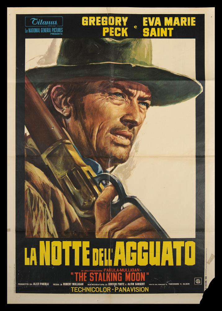 L'immagine riproduce uno dei manifesti conservati presso la Mediateca Regionale Pugliese (vedi Note). Si tratta di una delle versioni grafiche del manifesto del film “La notte dell’agguato”, del 1968 per la regia di Robert Mulligan. Il manifesto non presenta alcuna firma, ma lo stile utilizzato rispecchia le tendenze del tempo per la rappresentazione dei manifesti di film western. Lo spazio grafico è occupato solo dal mezzo busto del protagonista, la guida Sam Varner, interpretata da Gregory Peck. Il tratto è molto deciso e dettaglia ogni componente, dall’abbigliamento molto particolareggiato, al volto che evidenzia l’espressione rugosa e rude, divenendo uno degli sguardi più noti e caratteristici nel genere western. Da notare come l’espediente di una parte della falda ...