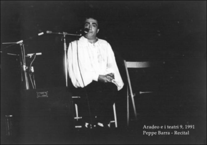 La fotografia in bianco e nero cattura un momento del recital interpretato nel 1991 dall'attore di teatro Peppe Barra durante la nona edizione di "Aradeo e i Teatri", un appuntamento con il teatro sperimentale che la compagnia nata nel 1983 nel piccolo borgo salentino di Aradeo porta avanti sin dall'anno della sua fondazione. L'artista, figlio d'arte nato a Roma, è espressione della canzone e del teatro di stampo napoletano, ai quali ha dedicato l'intera carriera di attore, solcando i palcoscenici italiani sin da bambino. Esibitosi nella villa comunale nuova di Aradeo durante la mini rassegna dedicata al teatro partenopeo, Barra ha incantato il pubblico con "Recital" e intonando alcune cantate prestigiose di autori come Raffaele Viviani e Salvatore Di Giacomo, mostrando...