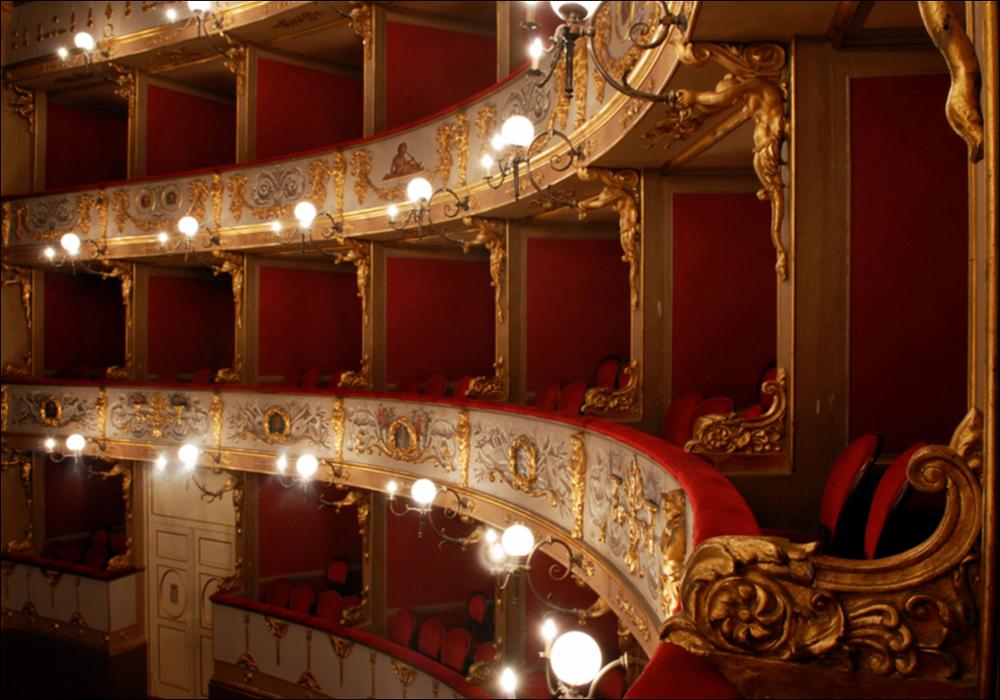 L'immagine è parte della campagna fotografica realizzata dalla fotografa Margherita Mirabella per Teatro Pubblico Pugliese, che con i suoi scatti ha ripreso le eleganti architetture e i rifiniti dettagli di alcuni dei più bei teatri pugliesi e di alcuni spettacoli teatrali portati in scena in questi ultimi anni. Lo scatto immortala un particolare della zona dei palchi laterali, all'interno di Teatro Curci di Barletta, importante contenitore culturale cittadino intitolato al compositore Giuseppe Curci situato in pieno centro. L'aspetto attuale è quello del nuovo teatro, costruito interamente sul precedente e più antico teatro di San Ferdinando, per volontà del comune, che lo acquistò ordinandone l'abbattimento dopo il suo crollo parziale. I lavori iniziarono nel 1868 con...