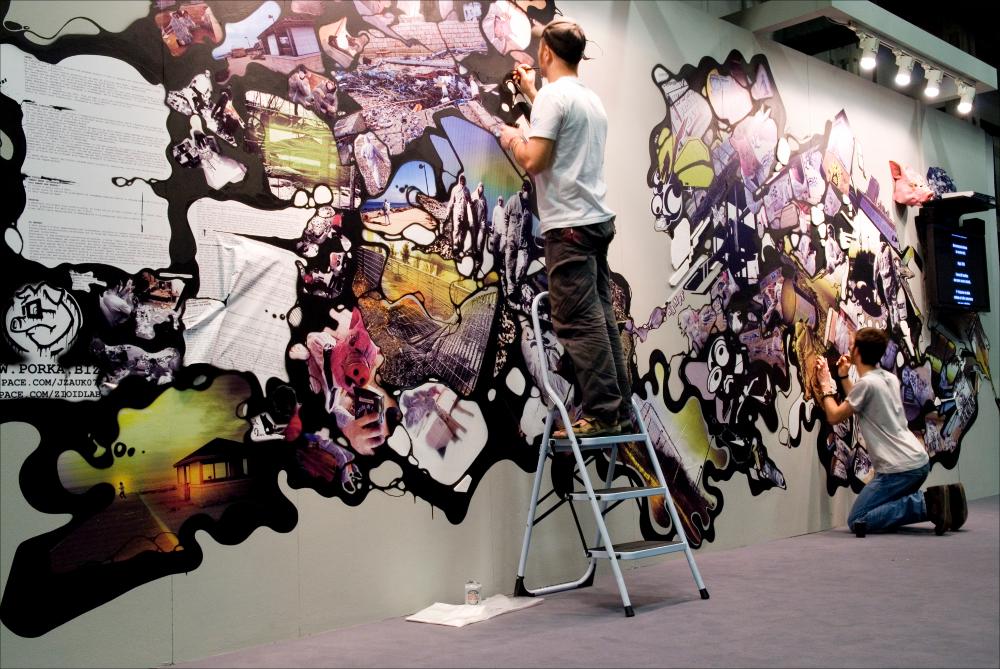 L'immagine digitale documenta un momento della "Biennale dei Giovani Artisti dell'Europa e del Mediterraneo", nella sua XIII edizione, fu ospitata in Puglia, a Bari, dal 22 al 31 maggio 2008 negli spazi della Fiera del Levante. La Biennale è considerata la più importante vetrina in Europa e nel Mediterraneo per la creatività delle giovani generazioni. Voluta da Regione Puglia e dall'Associazione Internazionale BJCEM e realizzata dal Teatro Pubblico Pugliese, la Biennale ha dato così spazio ad una visione multidisciplinare, multiforme e internazionalizzata dell'arte contemporanea attraverso creazioni di musica, arti visive, teatro, video, arti applicate, letteratura e gastronomia. Scattata a luce ambiente in uno degli spazi della Fiera, la fotografia rende un momento di ...