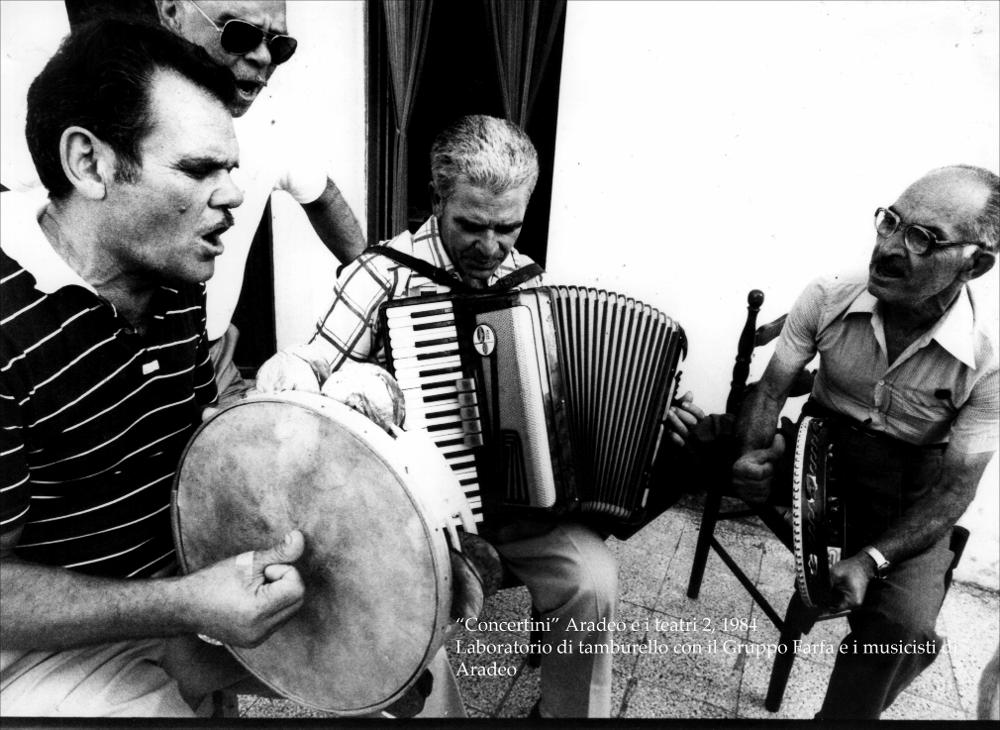 La fotografia in bianco e nero immortala un momento di formazione nell'ambito della rassegna annuale “Aradeo e i Teatri” del 1984, alla seconda edizione con il titolo “Concertini”, un appuntamento con il teatro sperimentale che la compagnia del Teatro Koreja, nata nel 1983 nel piccolo borgo salentino di Aradeo, porta avanti sin dall'anno della sua fondazione. Nello specifico si possono osservare diversi musicisti coinvolti nella manifestazione e componenti del gruppo teatrale ‘Gruppo Farfa', diretto dall'attrice danese Iben Nagel Rasmussen, intenti nello suonare alcuni strumenti. Si tratta di un vero e proprio laboratorio per apprendere le tecniche di utilizzo del tamburello, strumento principe della musica salentina, o meglio della pizzica. Spesso questo strumento è ac...
