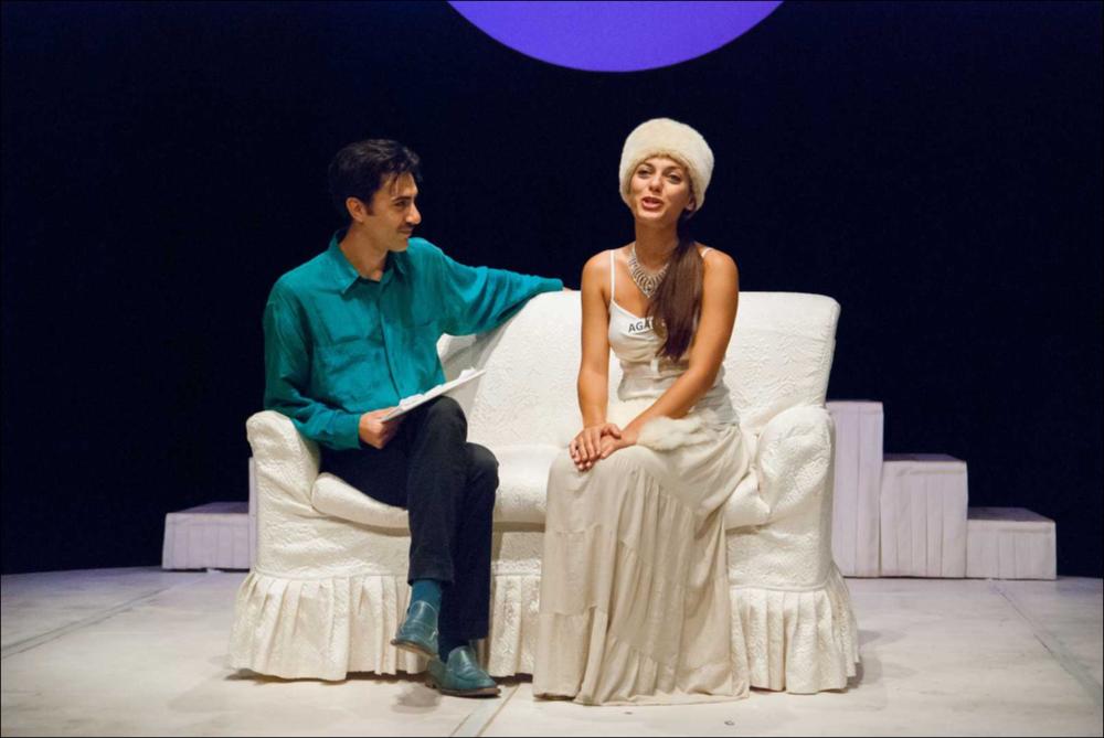 L'immagine in oggetto, fotografia digitale ad opera di Angela Chezzi, cattura un momento dello spettacolo “Il Matrimonio”, per la regia di Salvatore Tramacere, tratto dall'opera teatrale del 1842 di Nikolaj Vasil'evič Gogol', satira incentrata su una giovane donna, Agafija, corteggiata da quattro scapoli, ognuno con le sue eccentricità. Gli stessi personaggi vengono catapultati da Tramacere nel nostro tempo, portando con sé i lati più buffi e divertenti. Il palcoscenico ricorda un set di una trasmissione televisiva, con un presentatore che guida uomini e donne nella ricerca del partner, ma tutto risulta finto e lo schermo allontana ancor più i protagonisti, lasciandoli soli con le proprie inquietudini, aumentando così la distanza tra l'essere e l'apparire. Per far sposa...