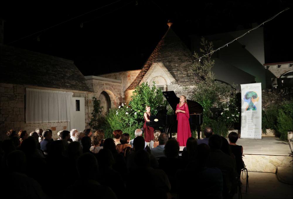 <div>Scatto del 23 luglio 2023, presso il <strong>Leonardo Trulli Resort</strong> di Locorotondo, dove una cantante dell’<strong>Accademia del Belcanto “Rodolfo Celletti” </strong>si esibisce accompagnata dal pianoforte, con alle spalle uno dei caratteristici <strong>trulli</strong>. L'esibizione fa parte del ciclo <em>Il Canto degli Ulivi</em>, inserito nella 49ª edizione del <strong>Festival della Valle d’Itria</strong>, e valorizza il bel canto e la tradizione vocale nella suggestiva cornice della Valle d’Itria.</div>...