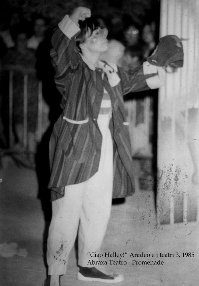 La fotografia in bianco e nero immortala un momento dello spettacolo fuori programma “Promenade”, messo in scena nel 1985 nell'ambito della rassegna annuale “Aradeo e i Teatri” giunta alla terza edizione con il titolo “Ciao halley - festeggiamenti per l'arrivo di una cometa”, un appuntamento con il teatro sperimentale che la compagnia Koreja, nata nel 1983 nel piccolo borgo salentino di Aradeo, porta avanti sin dall'anno della sua fondazione. La compagnia ‘Abraxa Teatro', fondata da Emilio Genazzini, portò per le strade di Aradeo una performance musico-teatrale itinerante, eseguita da acrobati, trampolieri, maghi, giocolieri e saltimbanchi, incantando un vasto pubblico che venne coinvolto attivamente nella messa in scena. Il programma prevedeva anche la rappresentazione...
