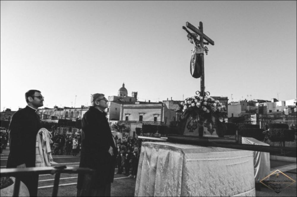 <div class="ql-editor"><div> Fotografia artistica che ritrae il <strong>Santissimo Crocifisso di Latiano</strong> preparato per la solenne processione dell’ultima domenica di agosto, momento centrale della festa dedicata al Crocifisso Redentore. Il venerato simulacro ligneo scuro, noto come <em>Crocifisso Nero</em> e custodito nella Chiesa del Santissimo Crocifisso, appare adornato e pronto per essere portato tra le vie della città. L’immagine evidenzia la forte devozione popolare che da secoli accompagna questo culto, profondamente radicato nella storia e nella spiritualità della comunità latianese. La scena restituisce il clima di raccoglimento e partecipazione che precede la processione, simbolo di fede condivisa e di identità colletti...