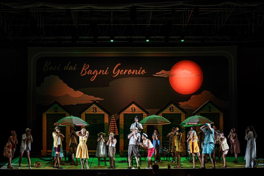 <div>Scena da<strong> <em>Il turco in Italia</em></strong> di Gioachino Rossini (18 luglio – 6 agosto 2023, Palazzo Ducale). L’opera buffa, proposta nella versione del 1815 e nell’edizione critica Ricordi curata per la Fondazione Rossini di Pesaro, è diretta da <strong>Michele Spotti</strong> con la regia di <strong>Silvia Paoli</strong>. La scenografia di <strong>Andrea Belli</strong> e i costumi di <strong>Valeria Donata Bettella</strong> ricreano un vivace ambiente balneare che caratterizza l’allestimento. In scena l’<strong>Orchestra</strong> e il <strong>Coro del Teatro Petruzzelli di Bari</strong>, con un cast guidato da Adolfo Corrado, Giuliana Gianfaldoni e Giulio Mastrototaro.</div>...