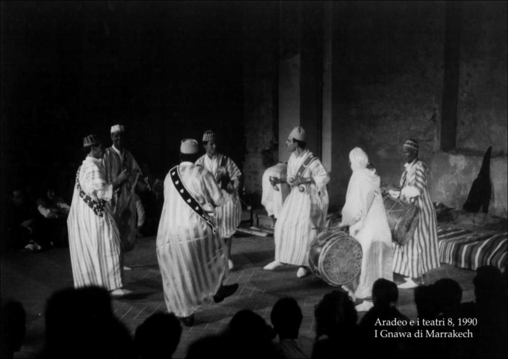 La fotografia in bianco e nero è un momento dello spettacolo tenuto nel 1990 dal Gruppo Gnawa durante l'ottava edizione di "Aradeo e i Teatri", un appuntamento con il teatro sperimentale che la compagnia Koreja nata nel 1983 nel piccolo borgo salentino di Aradeo porta avanti sin dall'anno della sua fondazione. I Gnawa, gruppo etnico proveniente dal Marocco e discendente dagli antichi schiavi africani, giunsero ad Aradeo per portare riti e spettacoli impregnati della loro cultura, nel nome della contaminazione culturale e teatrale, anima e scopo del festival salentino. La confraternita, dedita all'animismo e all'Islam, si esibì in danze rituali dal ritmo arcaico, gli stessi che loro usavano per evocare o respingere forze oscure. La tappa ad Aradeo costituì per il gruppo ...