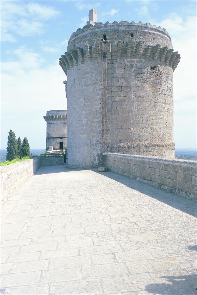 La fotografia è parte della ricca raccolta fotografica “Puglia per tutte le Stagioni” vol. 2, prodotta dall'Assessorato al Turismo e Industria Alberghiera della Regione Puglia, per raccontare la Puglia attraverso immagini suddivise in 5 settori principali: Città e Paesi, Settimana Santa, Territorio, Feste – Sagre – Tradizioni, Mercati – Prodotti – Cucina. L'immagine cattura una delle tre torri del Castello di Oria, cittadina in provincia di Brindisi, che costituiscono la caratteristica predominante di questo bellissimo gioiello in pietra fortificato. Costruito tra il 1225 e il 1233 per volere di Federico II, domina imponente tutta la cittadina dall'alto di Colle del Vaglio, con la sua forma a triangolo isoscele che ricorda un vascello. Delle tre torri, la Quadrata (o De...