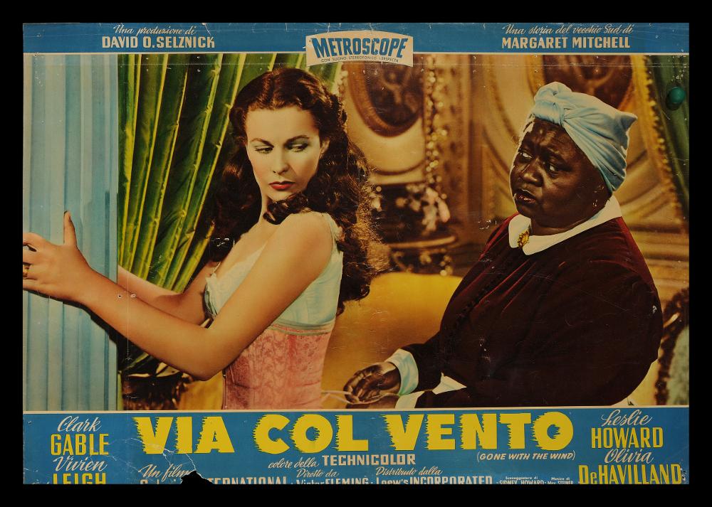 L'immagine riproduce uno dei manifesti conservati presso la Mediateca Regionale Pugliese (vedi Note). Si tratta di una delle fotografie di scena usate per le fotobuste del film "Via col vento" colossal del 1939 per la regia di Victor Fleming, adattamento cinematografico dell’omonimo romanzo di Margaret Mitchell del 1936. La scena si svolge tra le mure domestiche e vede protagoniste la bellissima Vivien Leigh, nei panni Rossella O'Hara volitiva figlia del proprietario di una piantagione della Georgia, e la fidata Mami interpretata da Hattie McDaniel, vincitrice del primo Oscar dato ad una donna di colore....