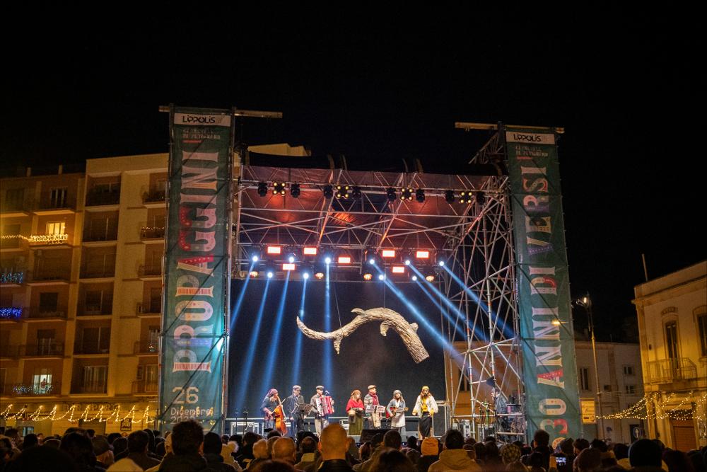 <p>La fotografia ritrae l’energia e l’ironia di “Le Propaggini”, il tradizionale festival in vernacolo che ha aperto la 630^ edizione del Carnevale di Putignano il 26 dicembre. Sul palco di Largo Porta Nuova, otto gruppi di poeti irridenti hanno animato il pubblico con rime pungenti e satira locale, celebrando l’antica tradizione contadina che da secoli anima la città. L’immagine cattura il momento in cui i propagginanti, tra costumi colorati e sorrisi contagiosi, portano avanti la festa che unisce storia, divertimento e spirito di comunità.</p>...