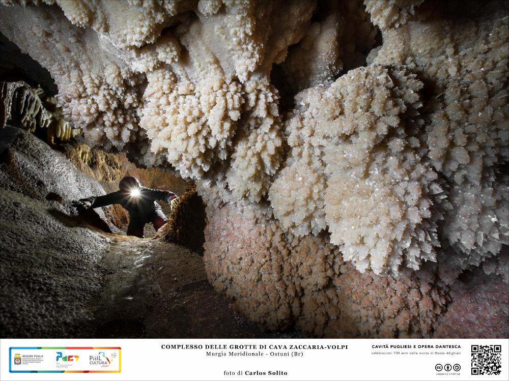 Siamo nel complesso delle Grotte di Cava Zaccaria-Volpi, nel territorio della bellissima Ostuni, nella Murgia meridionale. 
Discese e risalite in cunicoli angusti e tortuosi alla scoperta di un mondo sotterraneo silenzioso, popolato da infiorescenze bianchissime di concrezioni calcaree che sbocciano sulla roccia bagnata. Le grotte custodiscono gelosamente queste preziose opere d’arte naturali che l’acqua, nel corso dei millenni, ha saputo plasmare prodigiosamente.
L’immagine digitale fa parte della raccolta di fotografie prodotte da Carlos Solito per il Progetto digitale “Sillabario sotterraneo – Viaggio dantesco nelle Grotte di Puglia” – realizzato nell’ambito della LEGGE REGIONALE 30 dicembre 2020, n. 35 - art. 39 “Cavità pugliesi e opera dantesca - Celebrazioni 700 a...
