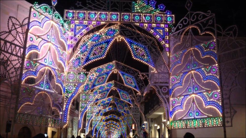 <div class="ql-editor"><div>Ripresa suggestiva che immortala il momento in cui le luminarie si accendono a sequenza, una dopo l’altra, creando un effetto scenografico di luce e movimento. Le arcate si illuminano progressivamente, disegnando nel buio motivi ornamentali che trasformano la strada in un corridoio luminoso, simbolo dell’inizio della Festa Patronale a Villa Castelli.</div><div><br></div><div>La Festa Patronale di <strong>Villa Castelli</strong> si svolge ogni anno dall’1 al 3 ottobre ed è uno degli appuntamenti più attesi e partecipati, non solo dai cittadini ma anche da tante persone provenienti dai paesi vicini. Conosciuta anche in dialetto come “Festa Bona”, è dedicata ai Santi Patroni, il Sacro Cuore di Ges...