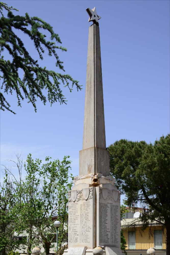 L'immagine è una veduta d'insieme del Monumento ai Caduti di Conversano. Ubicato nella zona centrale della città al termine della Villa comunale, il monumento fu concepito come una stele in pietra onoraria denominata col termine "Piramide in travertino", sulla cui sommità svetta una stella e fu realizzato dall'artista pugliese originario di Rutigliano Vitantonio De Bellis, autore di diversi monumenti sul territorio che divenne uno specialista del genere, un'attività fortunata che lo porterà poi a dedicarsi, negli anni '60-'70, al restauro e al reintegro dei suoi stessi monumenti.