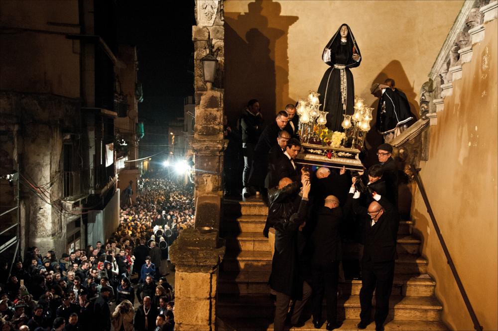 L'immagine digitale è scattata a luce ambiente durante uno dei momenti caratteristici dei riti della lunga Settimana Santa che nel periodo pasquale invade la città di Taranto di sacralità, tradizione e storia. La Settimana Santa, considerato tra gli eventi più importanti dell'anno a Taranto e in tutta la Puglia, inizia generalmente con la Domenica delle Palme, giornata nella quale si ricorda l'ingresso a Gerusalemme di Gesù Cristo salutato dal popolo con dei rametti di ulivo, simbolo di pace. I riti entrano nel vivo dell'atmosfera sacra dal giovedì Santo, giorno nel quale tutta la cittadinanza, profondamente coinvolta, rivive i momenti intensi della Passione di Cristo e dei dolori della Vergine Addolorata. Lo scatto cattura un dettaglio della processione dell'Addolorata...